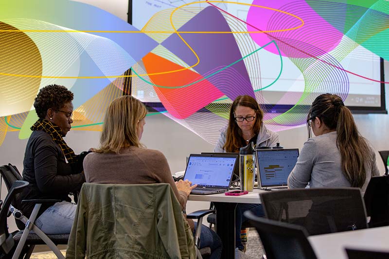 A picture of a group of people sitting around a table with computers with graphical elements behind them