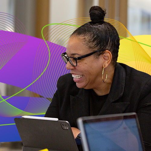 Image of a faculty member sitting at a desk with colorful graphics behind them